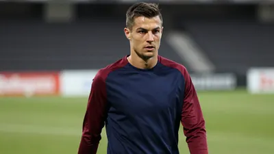 Mid-30s male footballer, athletic build, waist-up, wearing an unmarked navy shirt with claret sleeves, plain cotton...