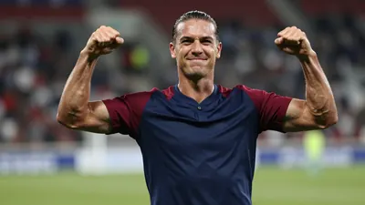 Mid-twenties forward, muscular, hair slicked back, eyes alight with triumph, navy shirt with claret sleeves, plain cotton...