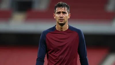 Mid-30s Sirius defender, gaunt, shoulders hunched, navy sleeves and claret torso plain training top, sweat-damp skin...