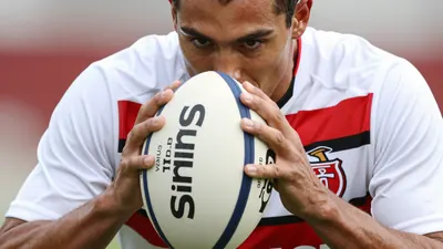 A close-up photo of an anonymous Sirius player holding the ball and looking focused, wearing a white jersey with red and...